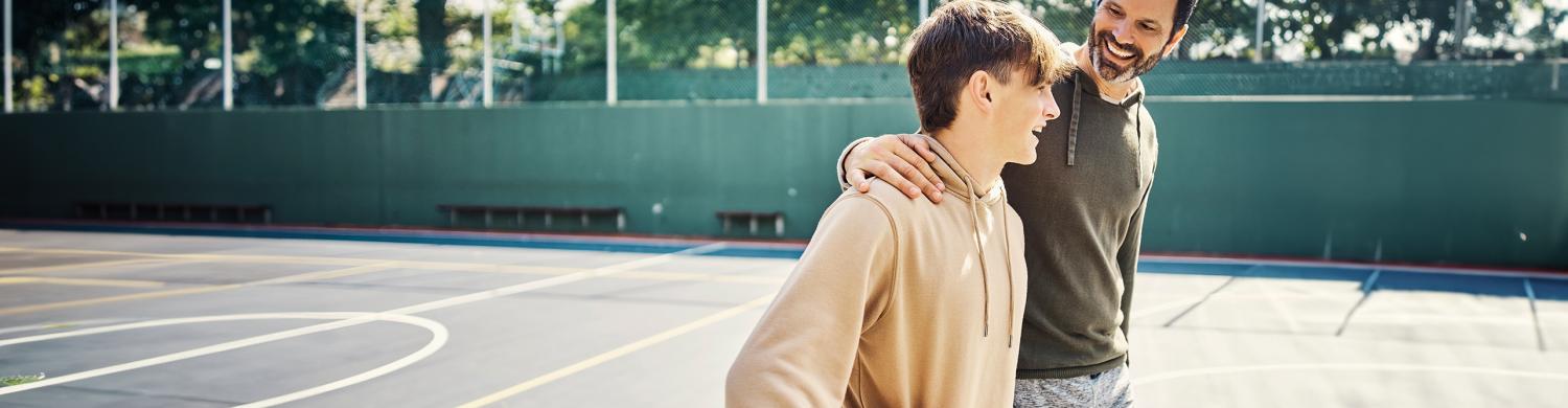 un père tenant l’épaule de son fils sur un terrain de basket