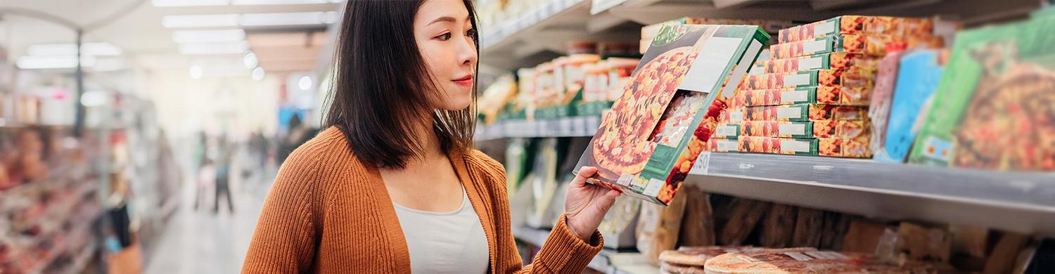 une femme choisit une pizza dans un rayon de supermarché