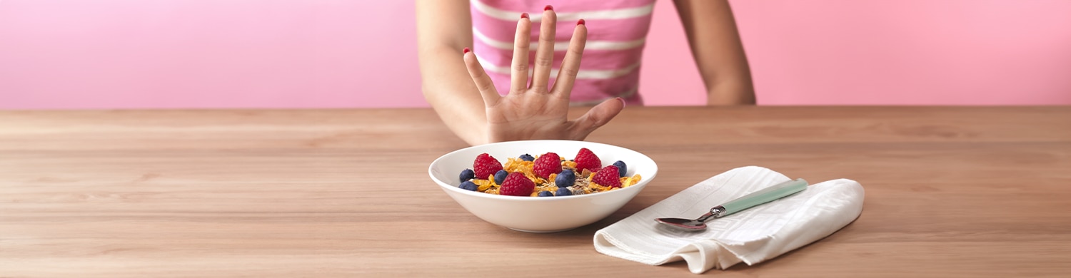 une  main qui repousse un bol de céréales et fraises