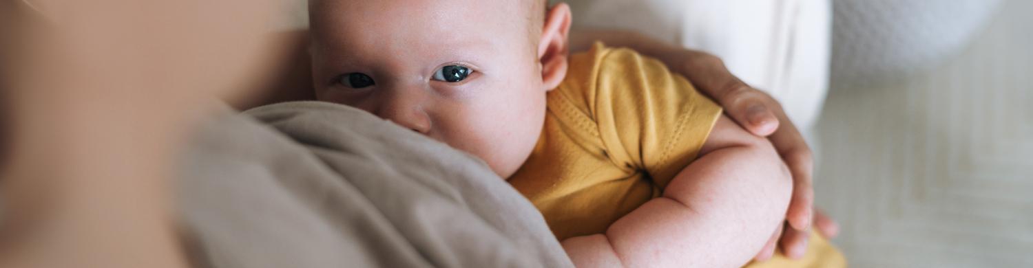 un bébé avec un body jaune en train de téter, qui regarde la caméra