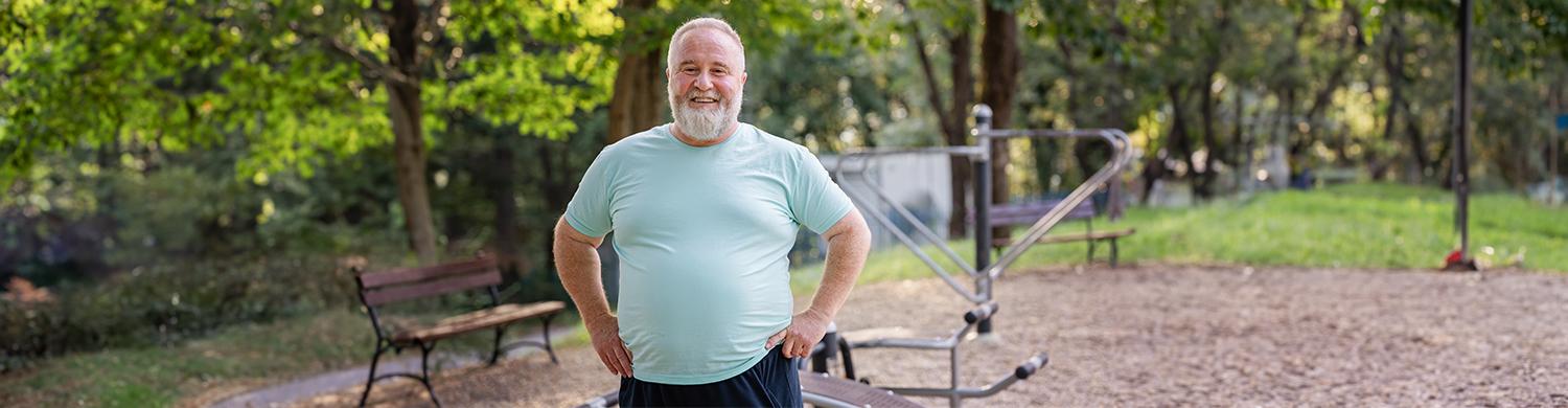 un homme blanc avec les cheveux et la barbe blanc et un teeshirt bleu ciel en surpoids avec qui sourit 