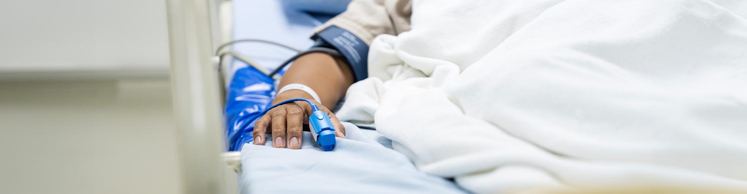 Bras qui dépasse d’un lit d’hôpital avec plusieurs câbles branchés