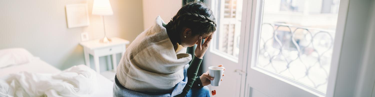 Une femme courbée, assise avec une tasse à la main devant une fenêtre