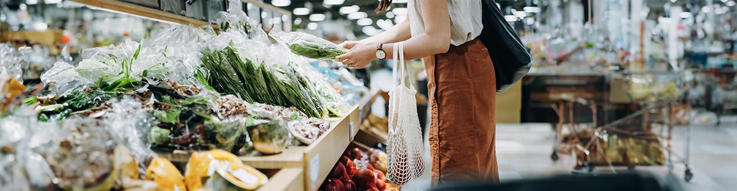 une femme avec un panier qui achète des légumes sur un étal de supermarché