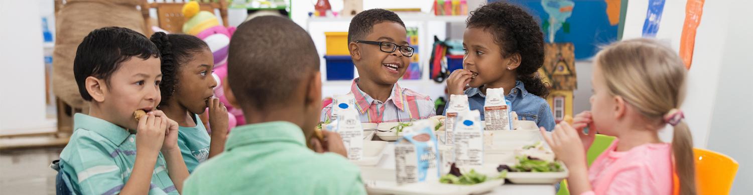 des enfants en train de déjeuner dans une cantine, souriants