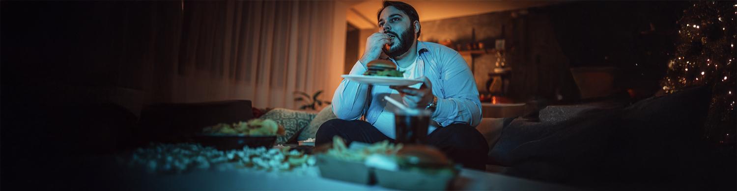un homme mange un burger devant un écran