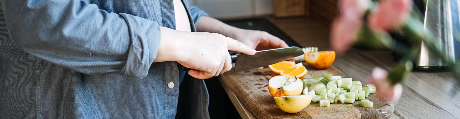 femme qui découpe des végétaux sur une planche en bois dans sa cuisine_bn