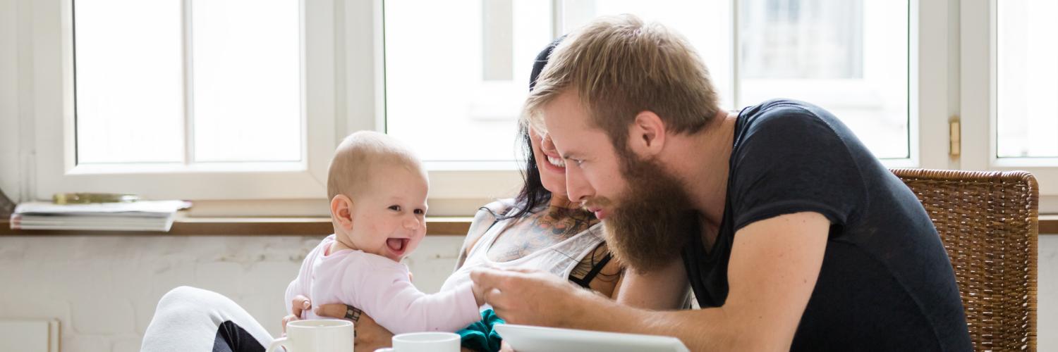 des parents et leur bébé sur les genoux sont à table avec une tablette