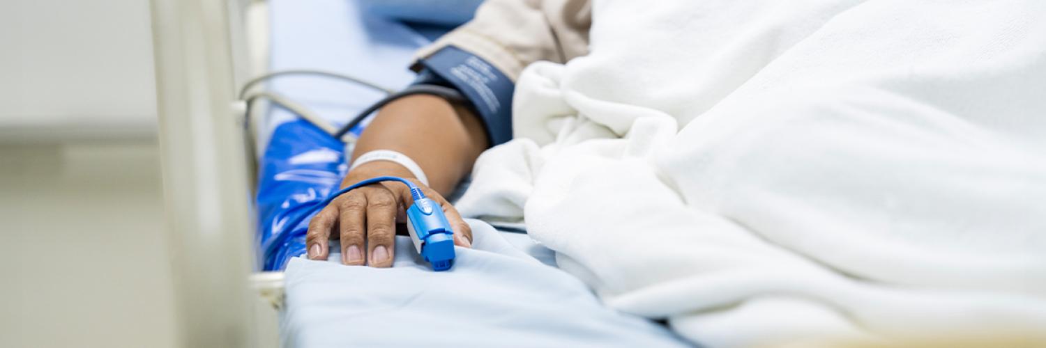 Bras qui dépasse d’un lit d’hôpital avec plusieurs câbles branchés