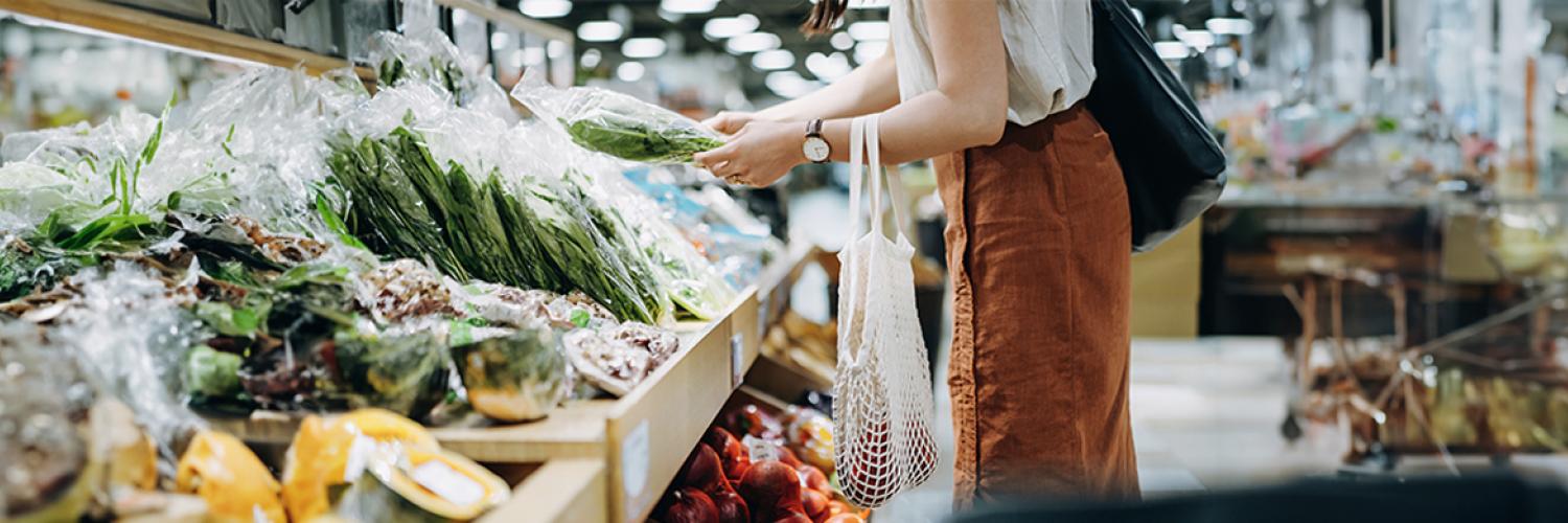 une femme avec un panier qui achète des légumes sur un étal de supermarché