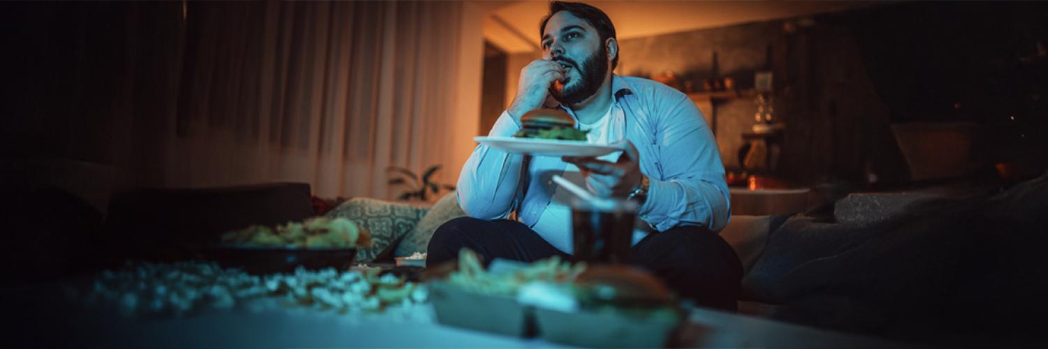 un homme mange un burger devant un écran