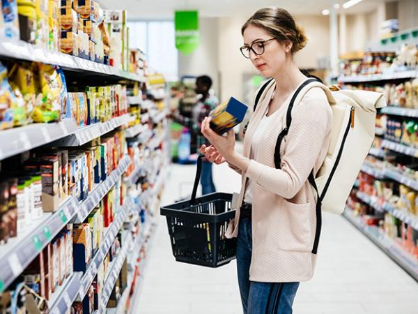 une dame avec des lunettes dans un rayon de supermarché qui regarde le dos d’un produit