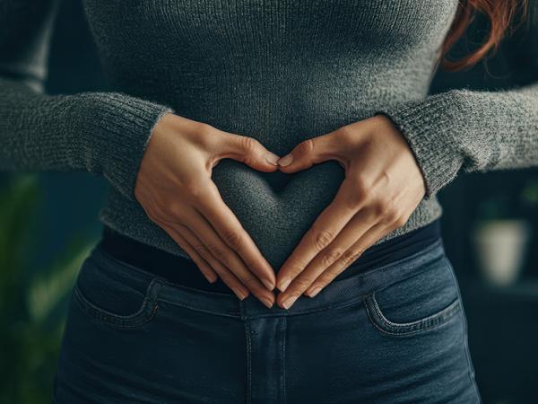 femme tient ses mains en cœur sur son ventre