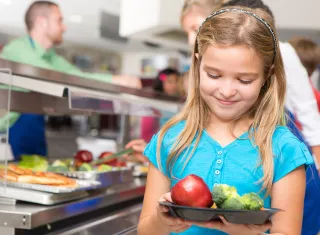 une enfant dans une cantine scolaire avec des légume