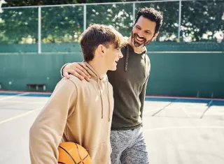 un père tenant l’épaule de son fils sur un terrain de basket