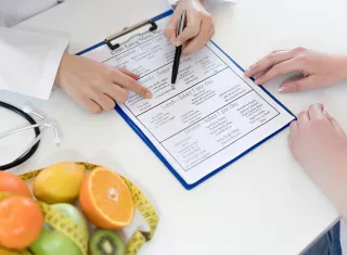 des mains qui pointent un document, une corbeille de fruits à côté