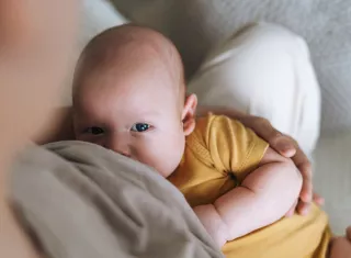 un bébé avec un body jaune en train de téter, qui regarde la caméra