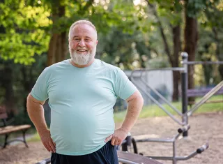 un homme blanc avec les cheveux et la barbe blanc et un teeshirt bleu ciel en surpoids avec qui sourit 
