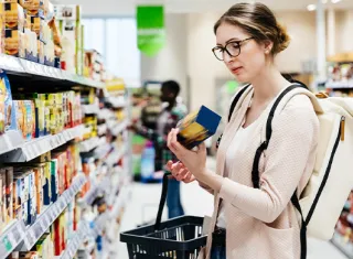 une dame avec des lunettes dans un rayon de supermarché qui regarde le dos d’un produit