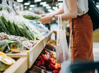une femme avec un panier qui achète des légumes sur un étal de supermarché