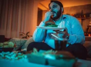 un homme mange un burger devant un écran
