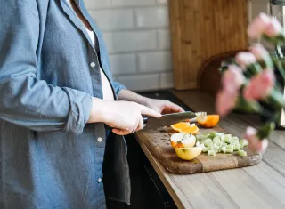femme qui découpe des végétaux sur une planche en bois dans sa cuisine