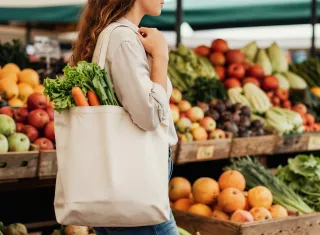 femme dans un rayon de fruits et légumes avec un sac de course à la main